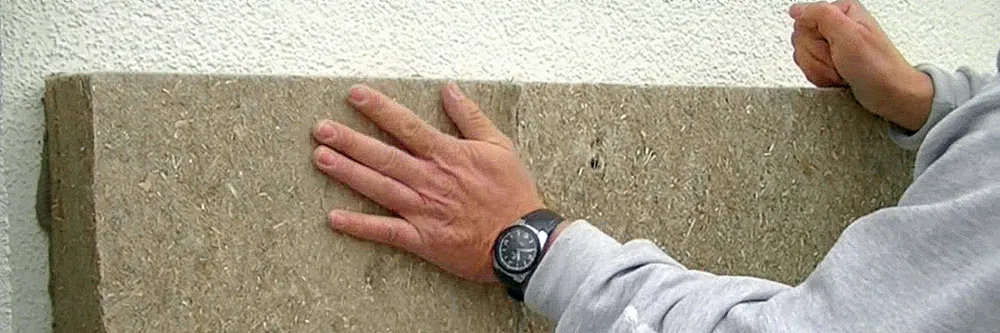 Hände setzen eine Holzfaser-Dämmplatte an der Fassade an